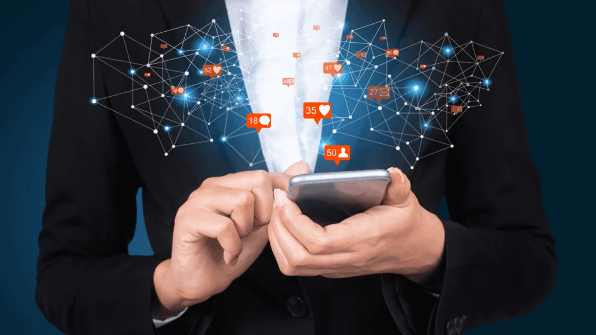 Person in a business suit holding a smartphone with floating social media notification icons and network connections radiating outward. The image represents digital communication social engagement and connected data networks.