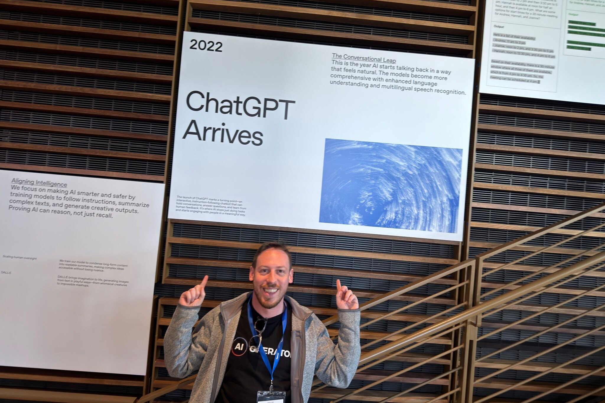 Tim Cakir in an AI Operator t-shirt and conference lanyard, pointing up at an exhibition panel headed 2022 — ChatGPT Arrives.